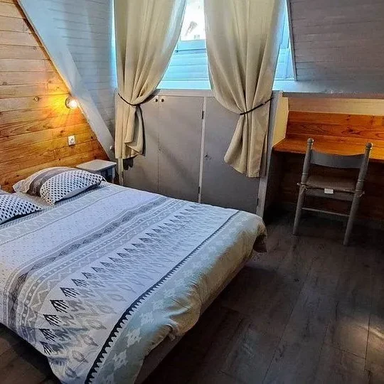 Chambre 2 personnes Chambre cosy avec lit double, bureau et rideaux, murs en bois clair.